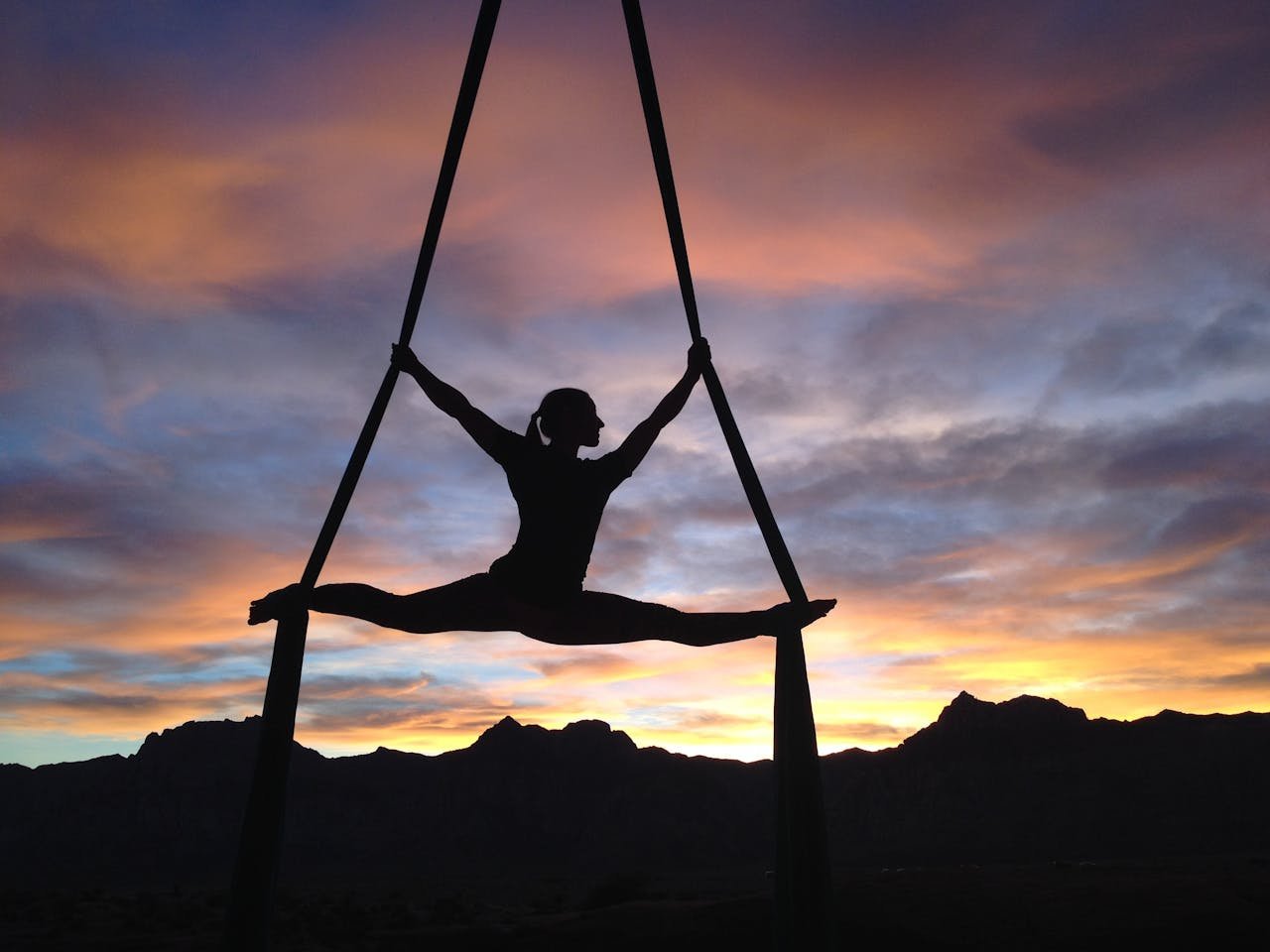 about-us-02 Silhouette of a woman practicing aerial yoga against a vibrant sunset sky in Las Vegas.